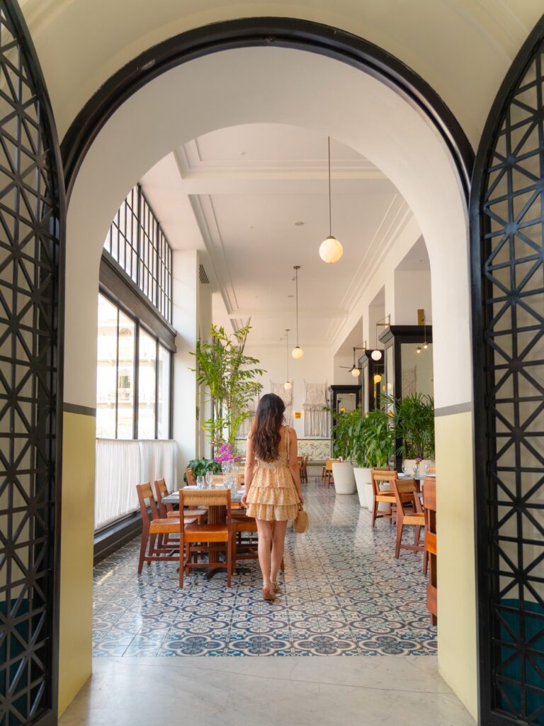 Woman walking through arched doorway into the light-filled restaurant at American Trade Hotel with blue patterned tile floor, Casco Viejo Panama