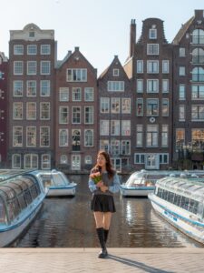 Woman holding tulips in front of the iconic canal houses and tour boats in Amsterdam