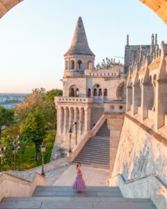 Woman in purple dress walking up the stone stairs of Fishermans Bastion in Budapest at sunrise