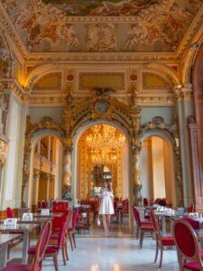 Woman walking through the ornate gold baroque interior of the New York Cafe in Budapest