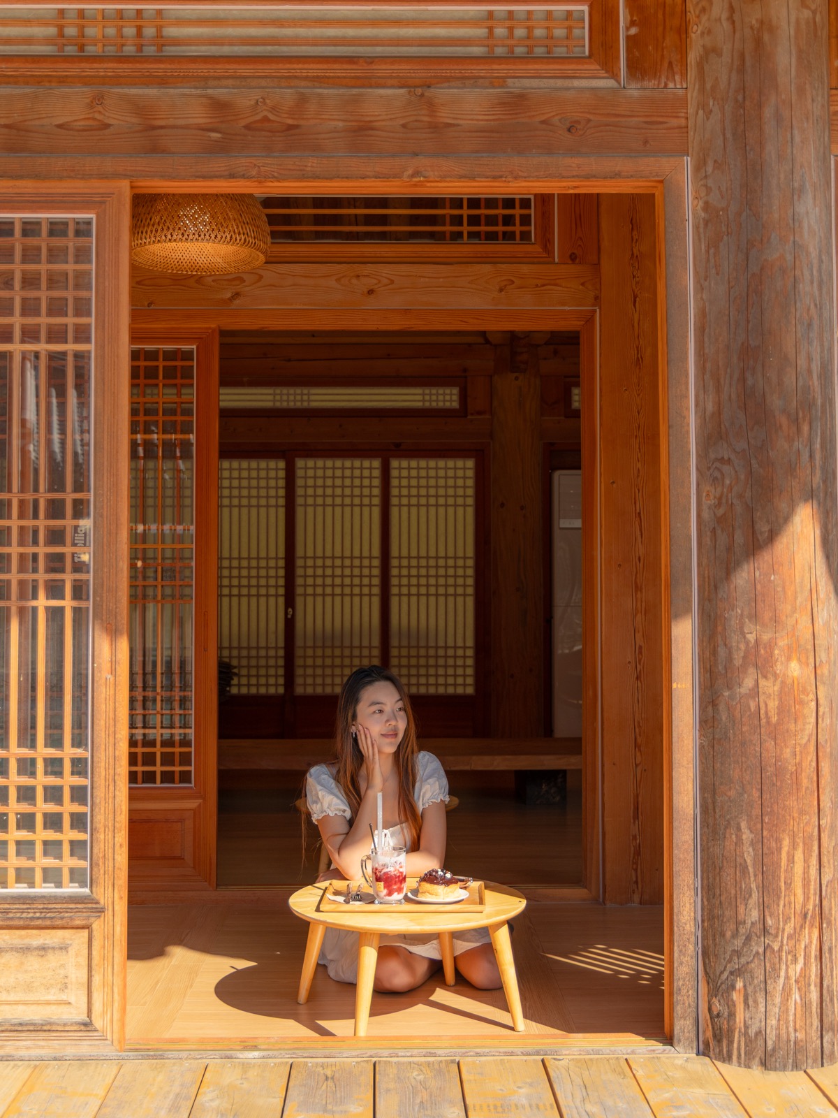 Woman sitting in the doorway of a traditional hanok at Cafe Tirol with a tea and dessert tray on a small wooden table