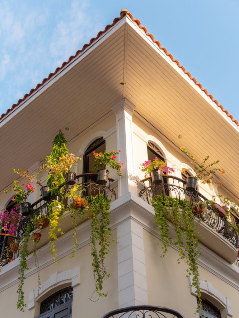 Corner of a cream-colored colonial building with flower-draped wrought iron balconies and a red tile roof in Casco Viejo Panama