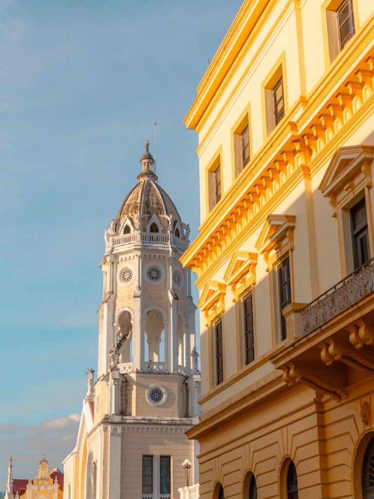 The white clock tower of the Metropolitan Cathedral at golden hour beside a yellow neoclassical building in Casco Viejo Panama
