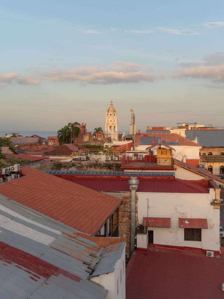 View from a rooftop in Casco Viejo at sunset with the Metropolitan Cathedral tower and red tile rooftops visible against the sky