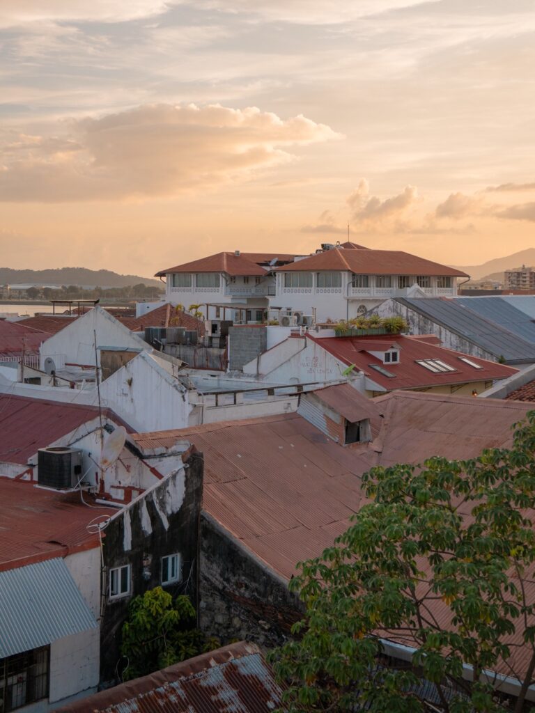 View from a rooftop in Casco Viejo at sunset looking over colonial rooftops toward the bay and distant hills