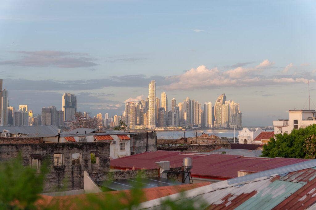 View from a rooftop in Casco Viejo across red tin rooftops to the modern Panama City skyline at golden hour