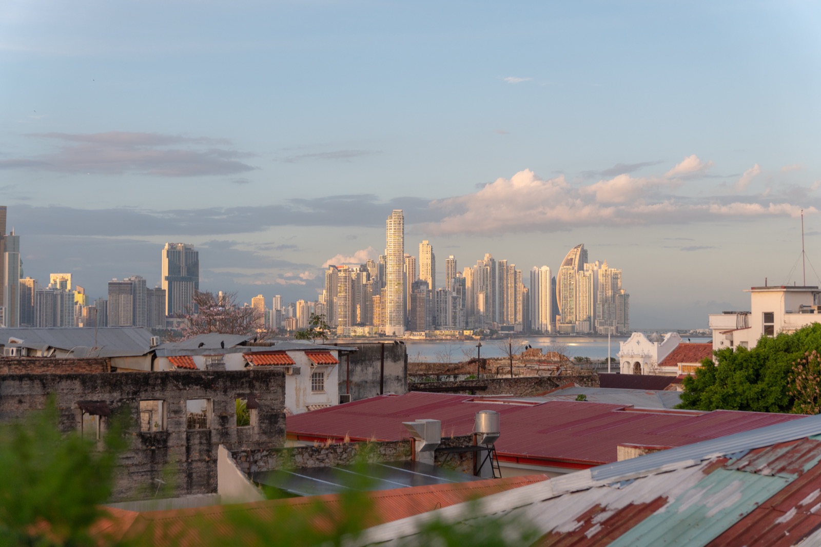 View from a rooftop in Casco Viejo across red tin rooftops to the modern Panama City skyline at golden hour
