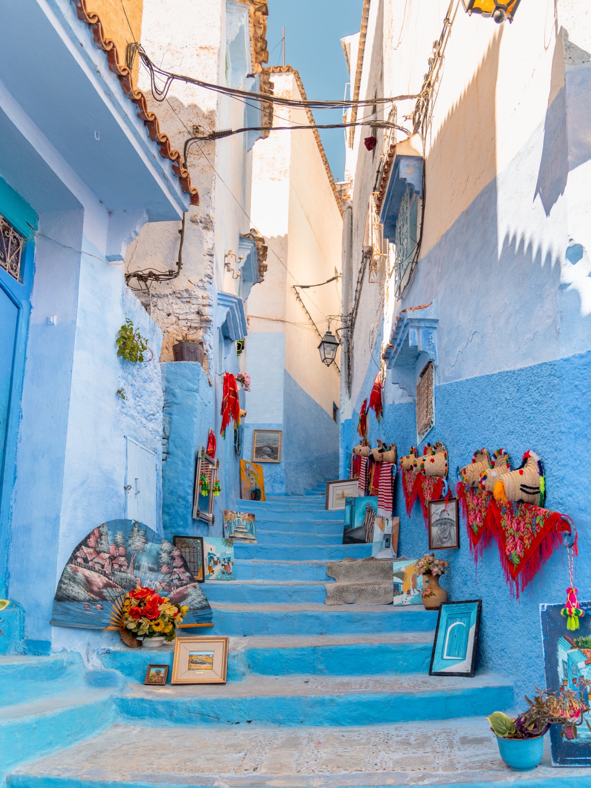 Blue steps lined with local artwork and woven goods in Chefchaouen’s medina