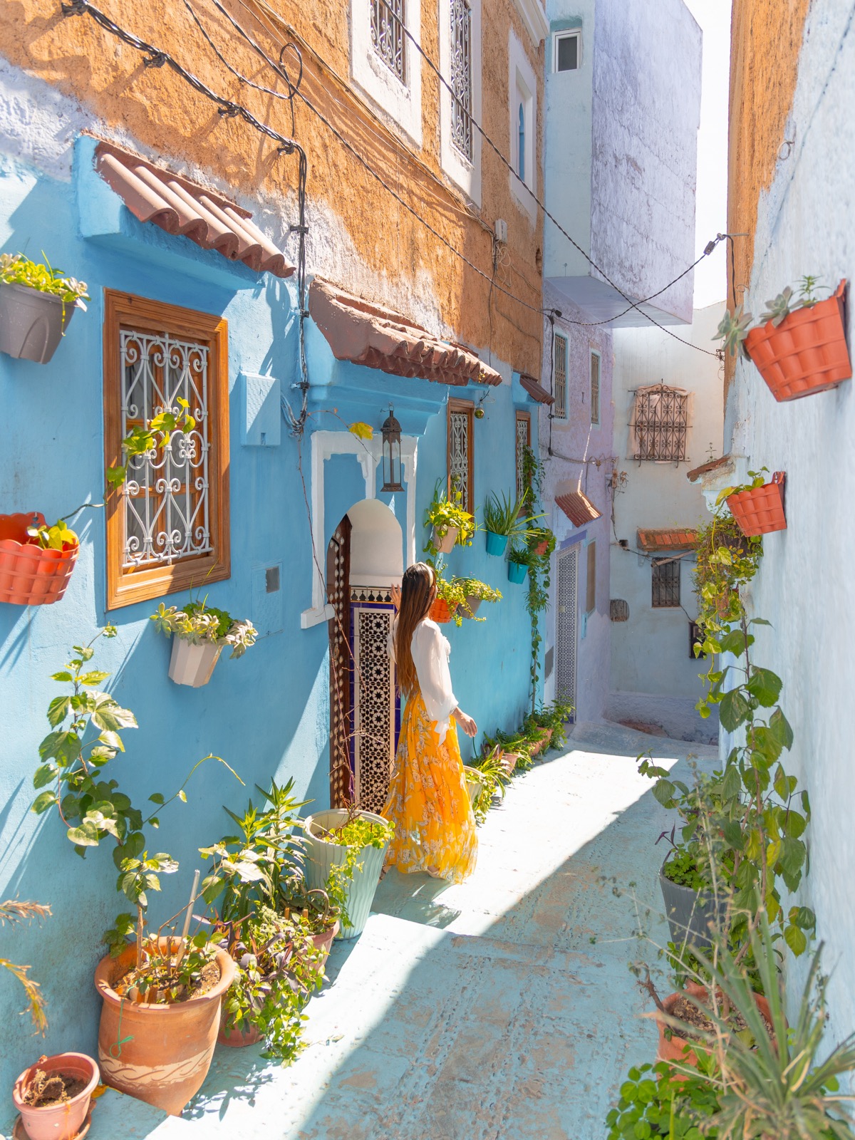 Amy walking beside colorful flowerpots in a blue Chefchaouen medina alley