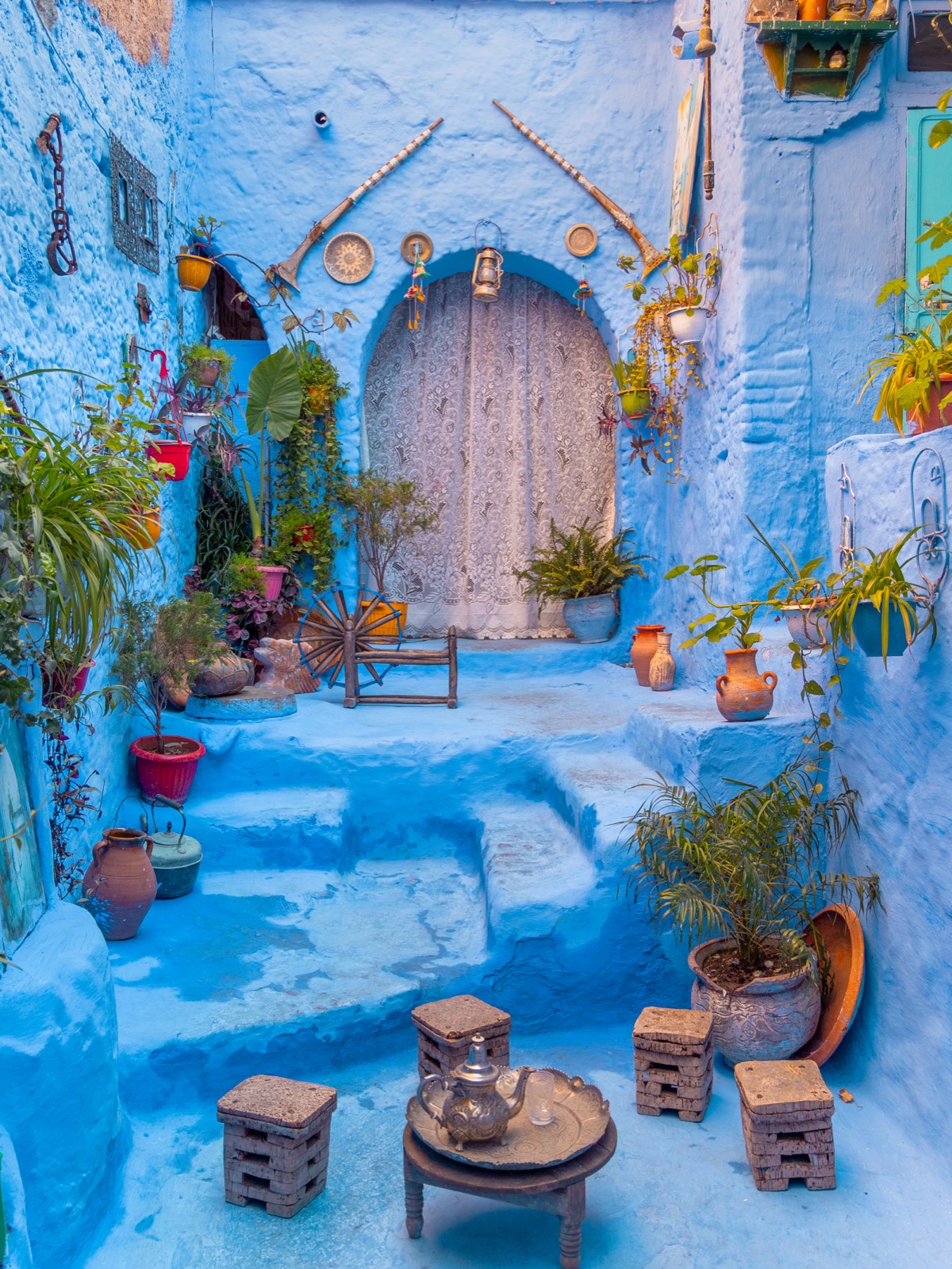 A decorated blue courtyard with plants, pottery, lanterns, and a tea tray in Chefchaouen