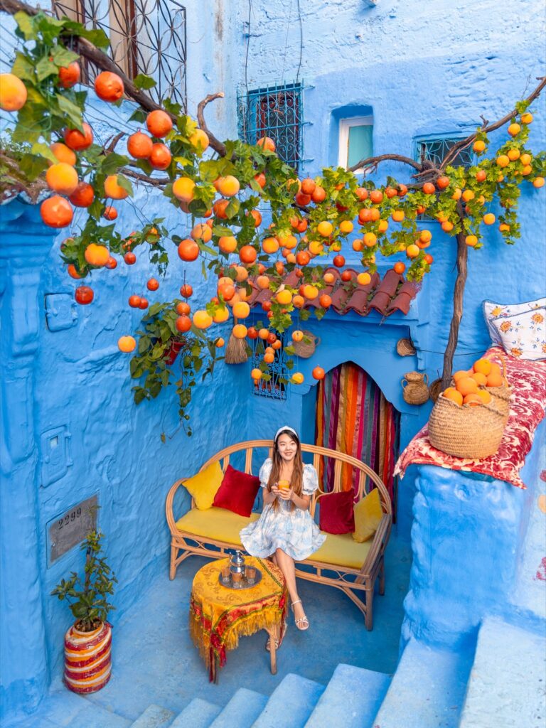 Amy seated with fresh orange juice beneath an orange tree in a blue Chefchaouen courtyard