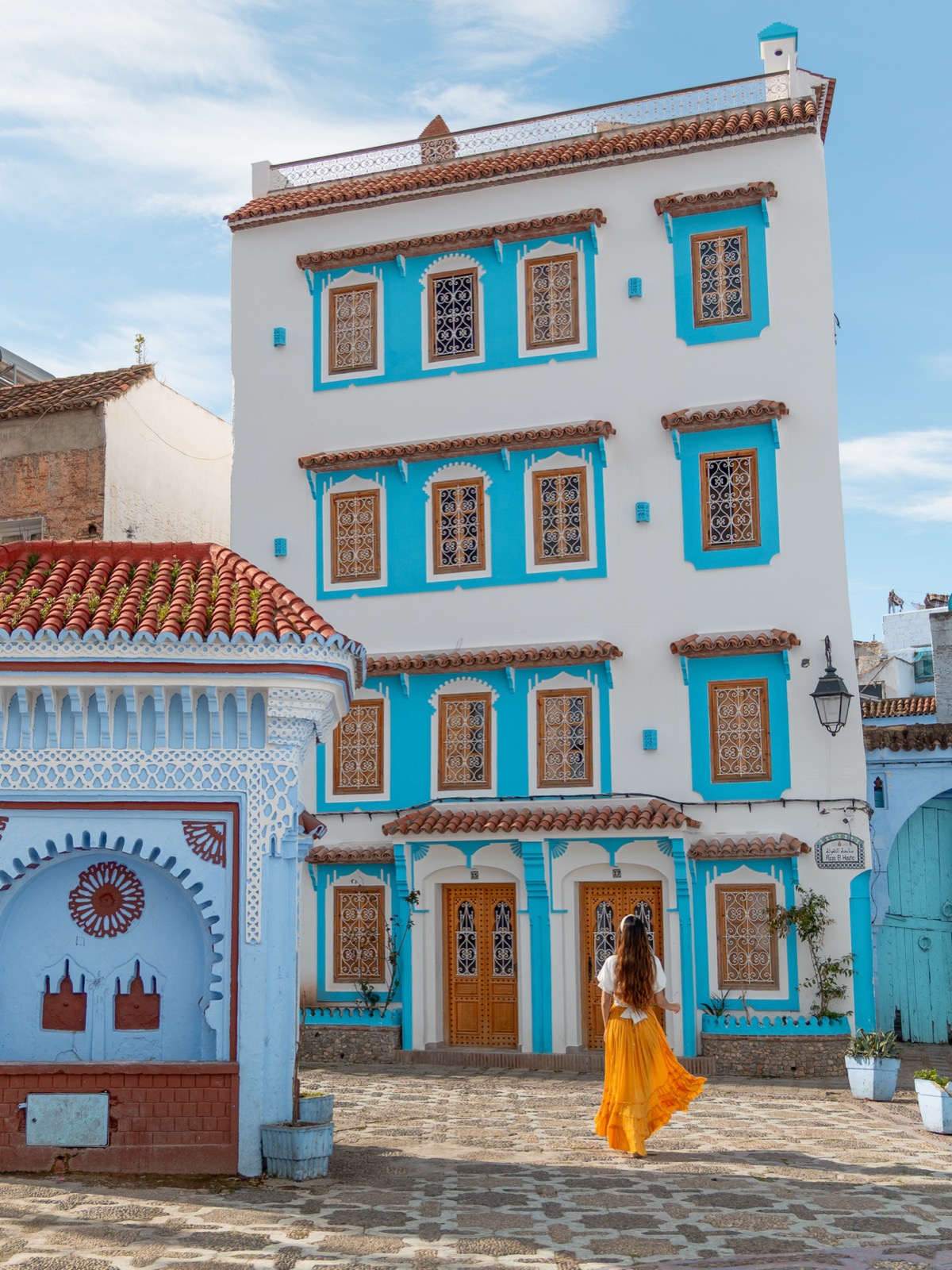 Amy in a yellow skirt walking through Place El Haouta in Chefchaouen, Morocco