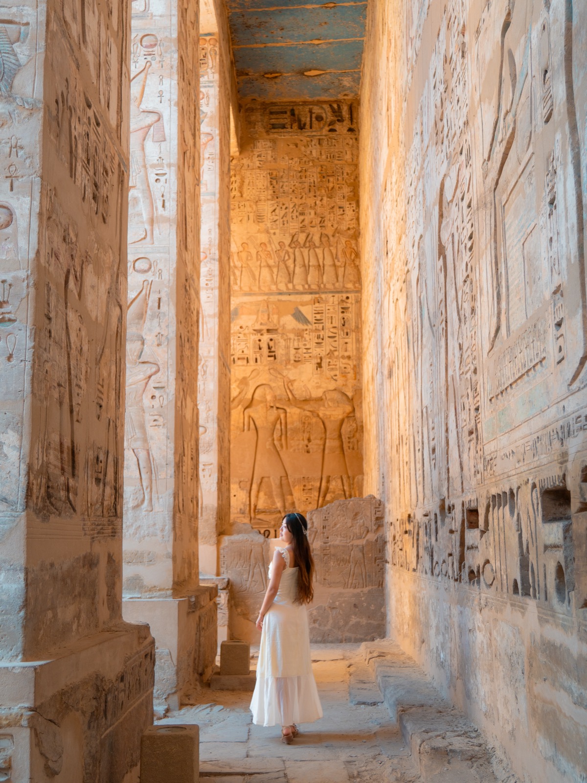 Woman walking through carved reliefs at Medinet Habu in Luxor