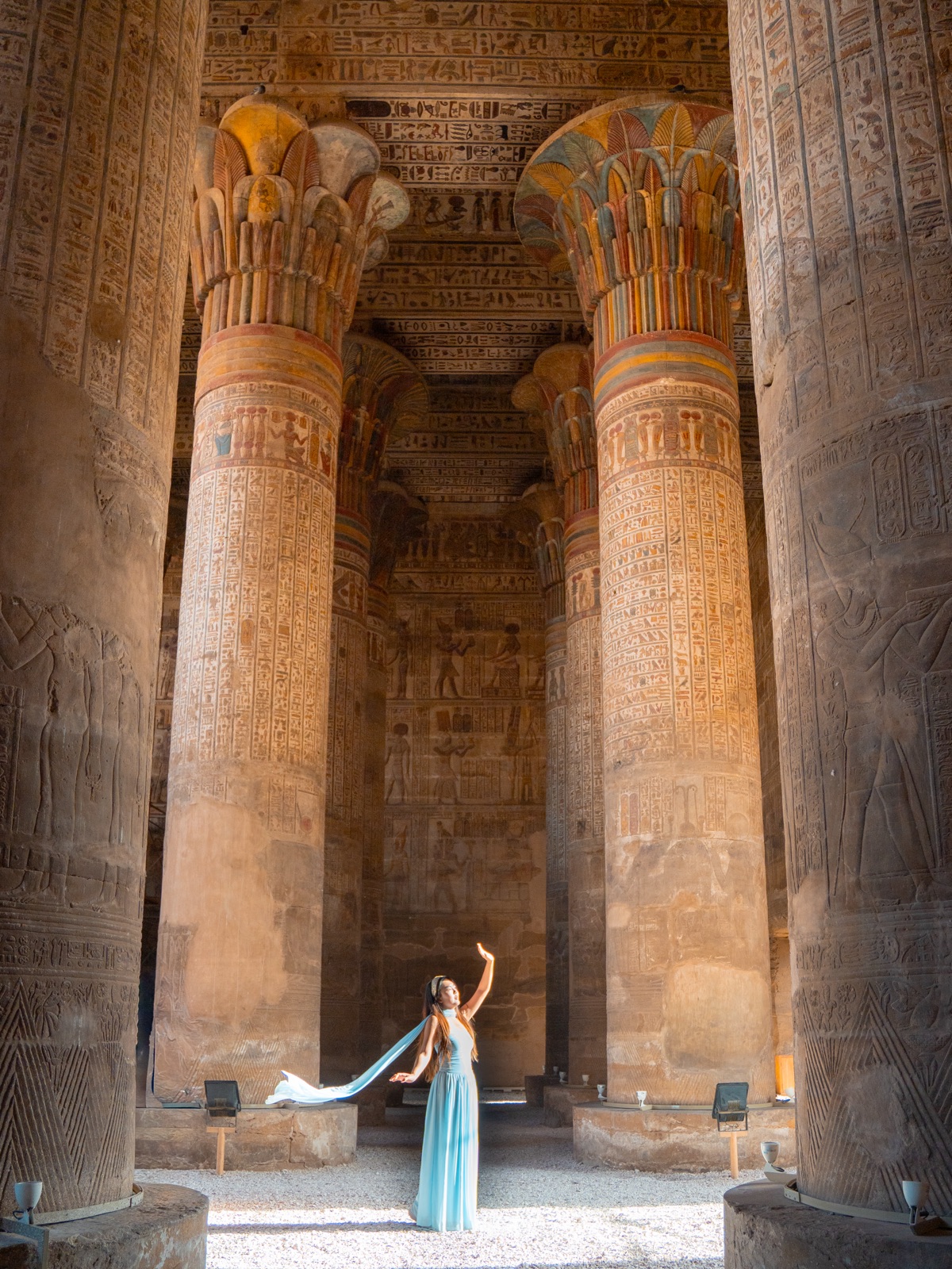 Woman standing between painted columns at Esna Temple in Egypt