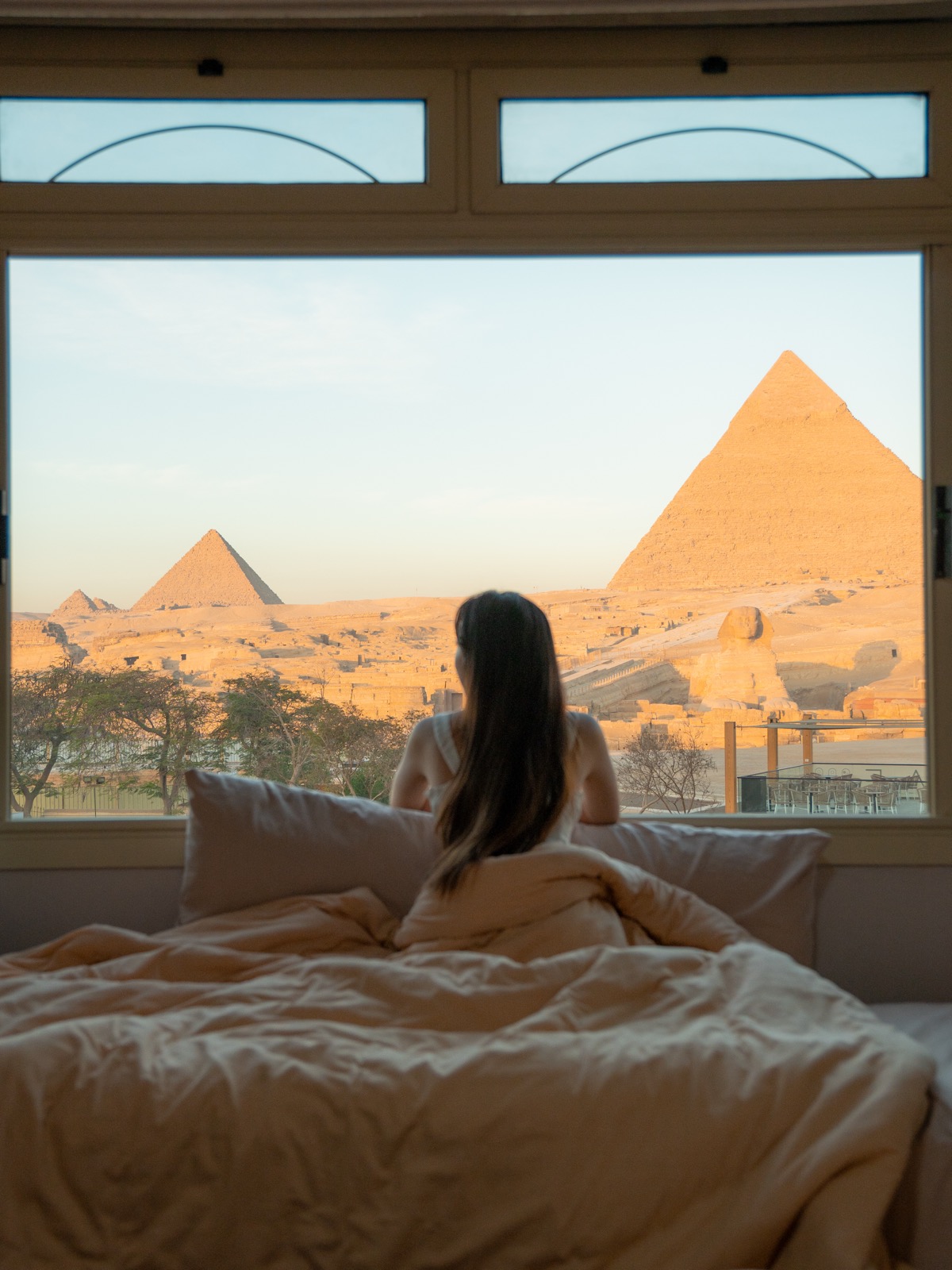 Amy sitting on a bed facing the Pyramids of Giza at sunrise from Guardian Guest House