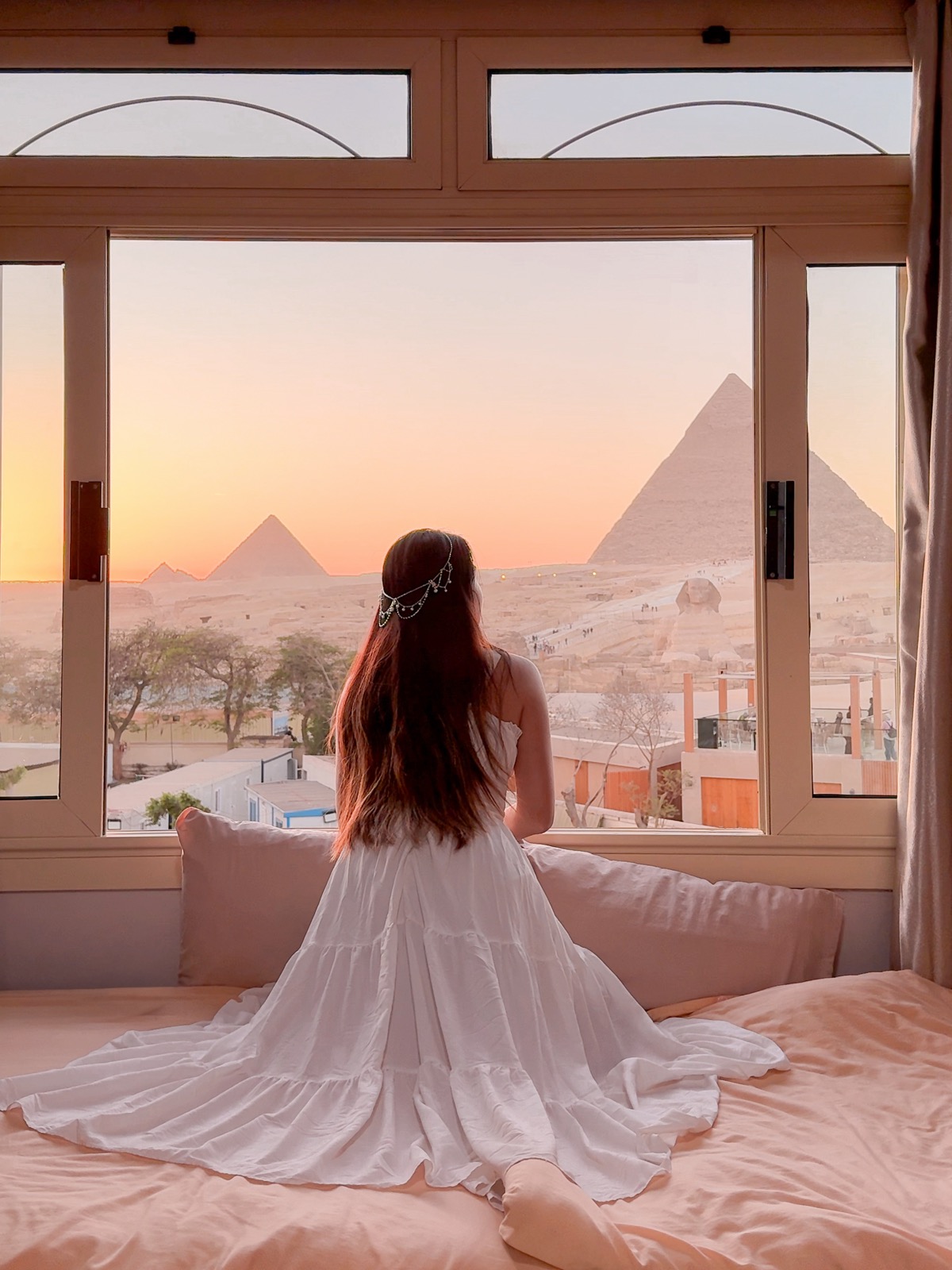 Amy sitting on a bed at Guardian Guest House with the Pyramids of Giza at sunset