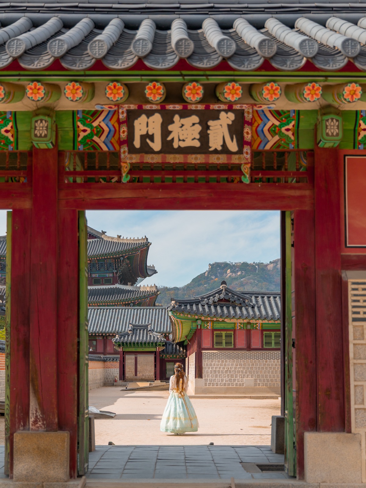 Woman in hanbok perfectly framed by one of the ornate painted gates of Gyeongbokgung Palace in Seoul, South Korea