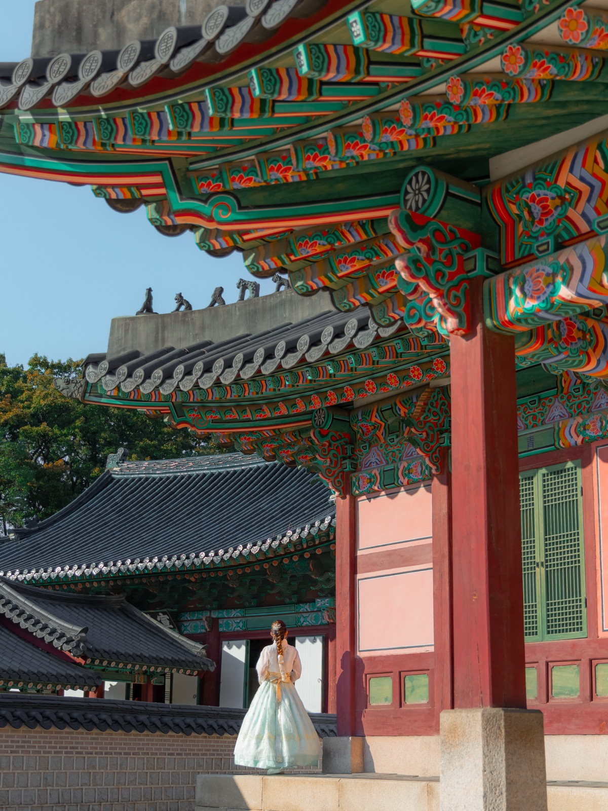 Woman in hanbok standing beneath the colorful painted eaves of Gyeongbokgung Palace in Seoul, South Korea