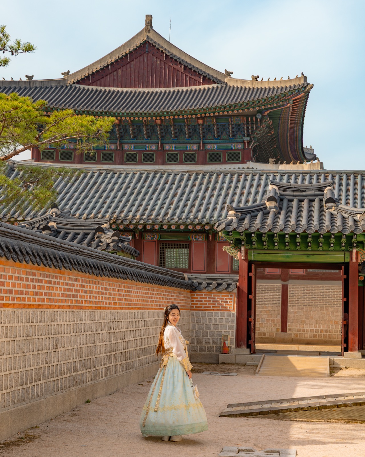 Woman in hanbok smiling in the courtyard of Gyeongbokgung Palace with the main hall visible behind her in Seoul, South Korea