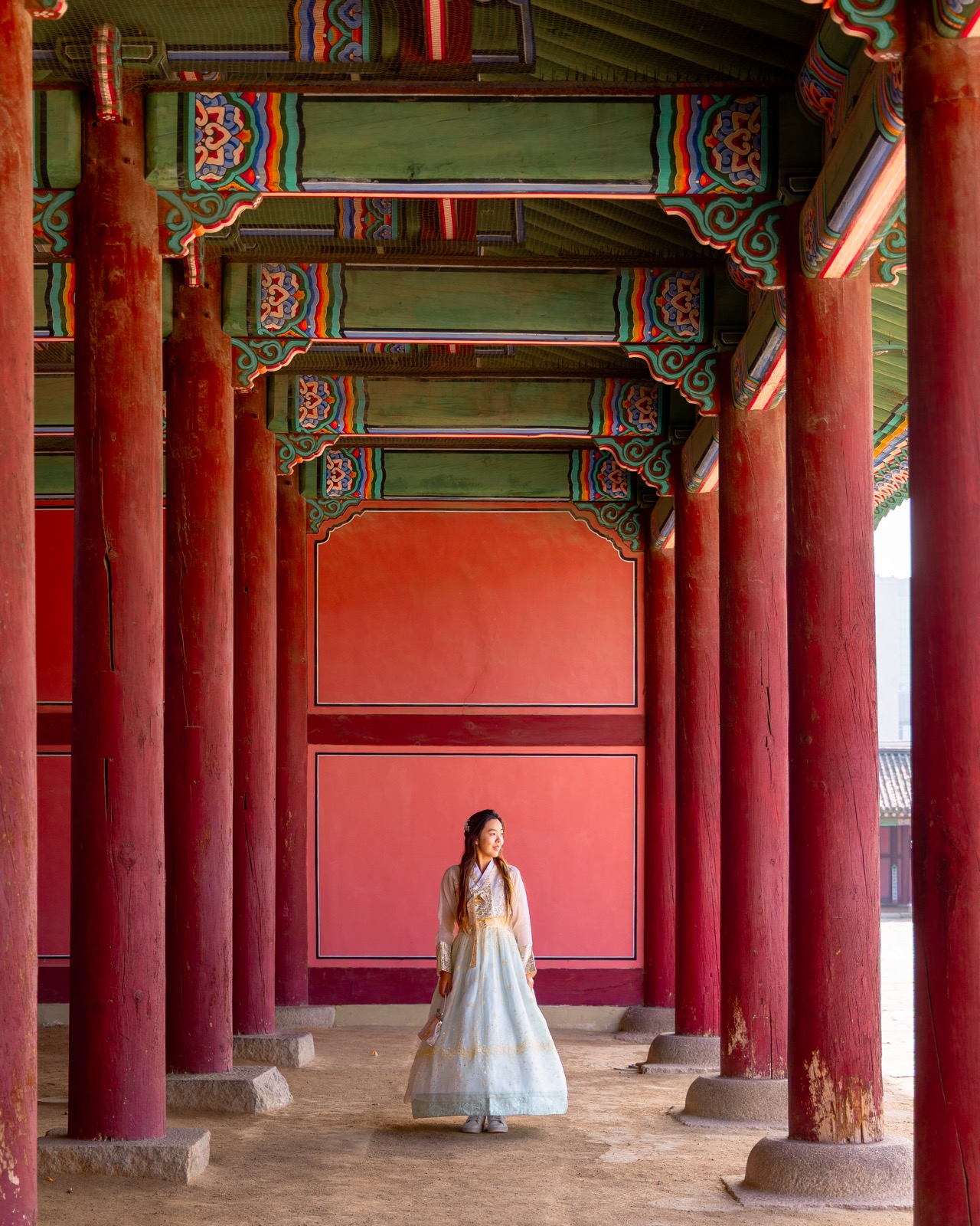 Woman in hanbok walking through the striking red column corridor at Gyeongbokgung Palace in Seoul, South Korea