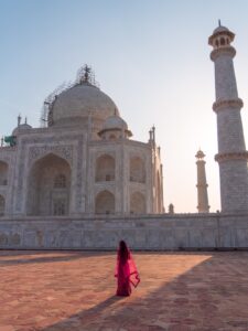 Woman in red sari walking toward the Taj Mahal at sunrise in Agra, India