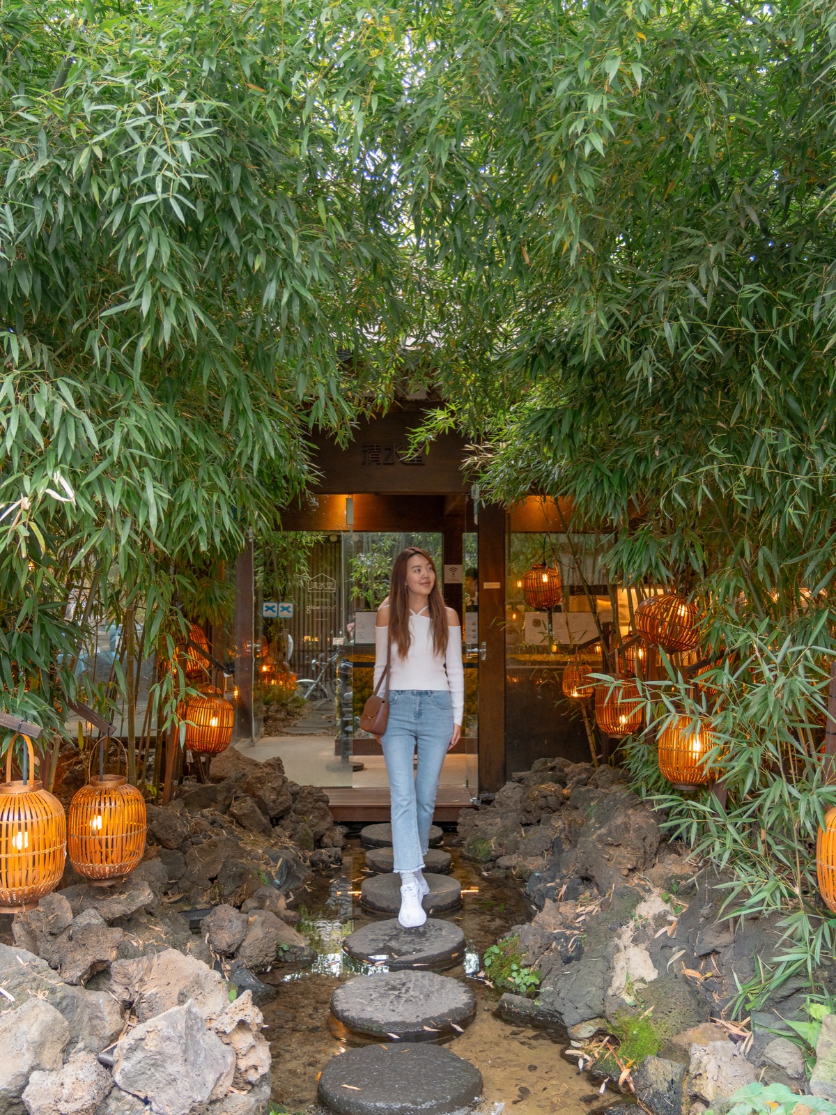 Woman walking through a bamboo garden with stepping stones and warm lantern lights at a traditional Korean cafe in Seoul, South Korea