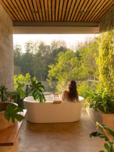 Woman relaxing in an open-air bathtub surrounded by tropical plants overlooking the jungle at Kafen Hotel in El Salvador