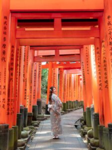 Woman in kimono standing inside the vermillion torii gate tunnel at Fushimi Inari Shrine