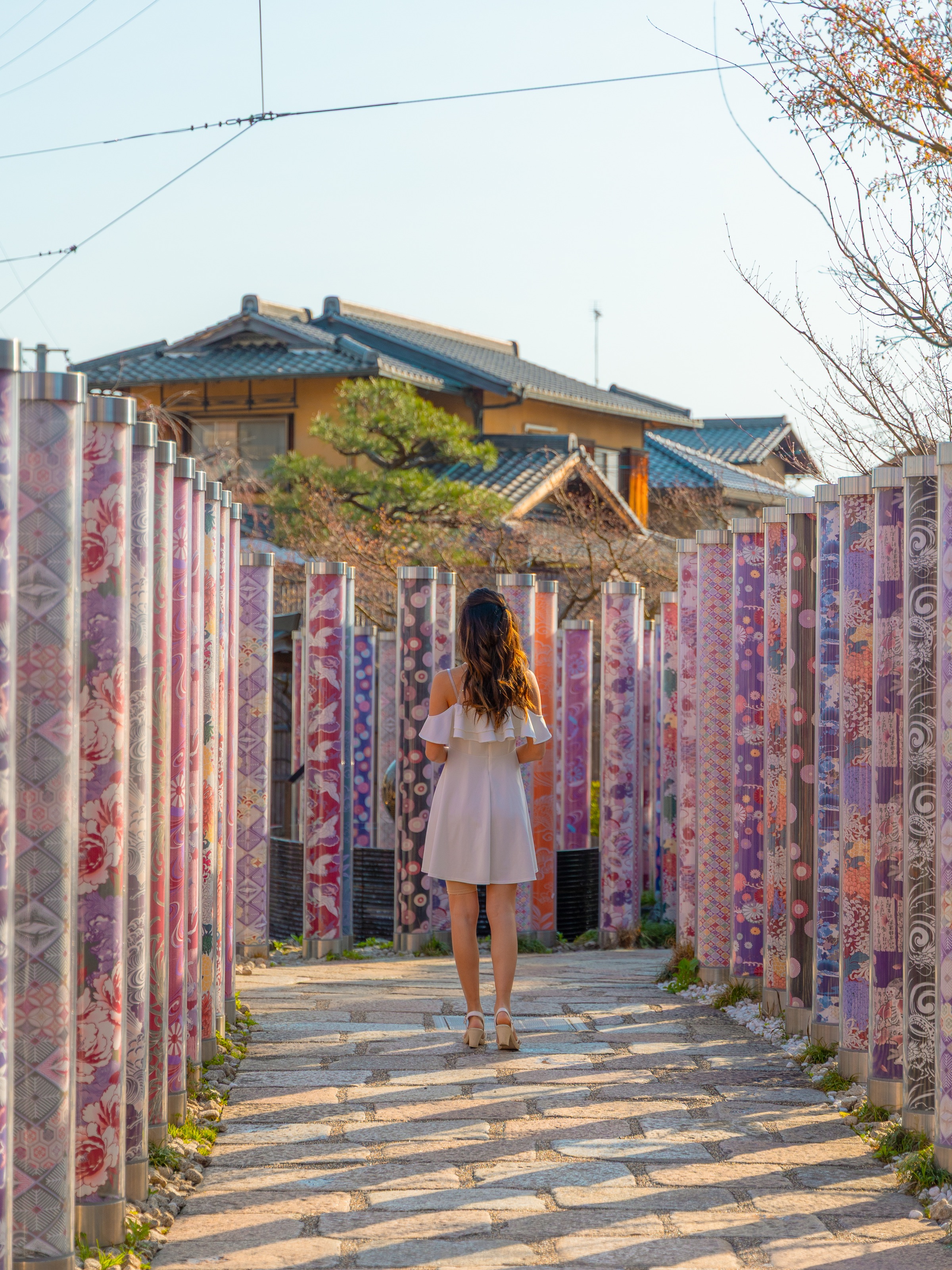 Woman walking away between rows of kimono fabric pillars at the Kimono Forest in Arashiyama, Kyoto