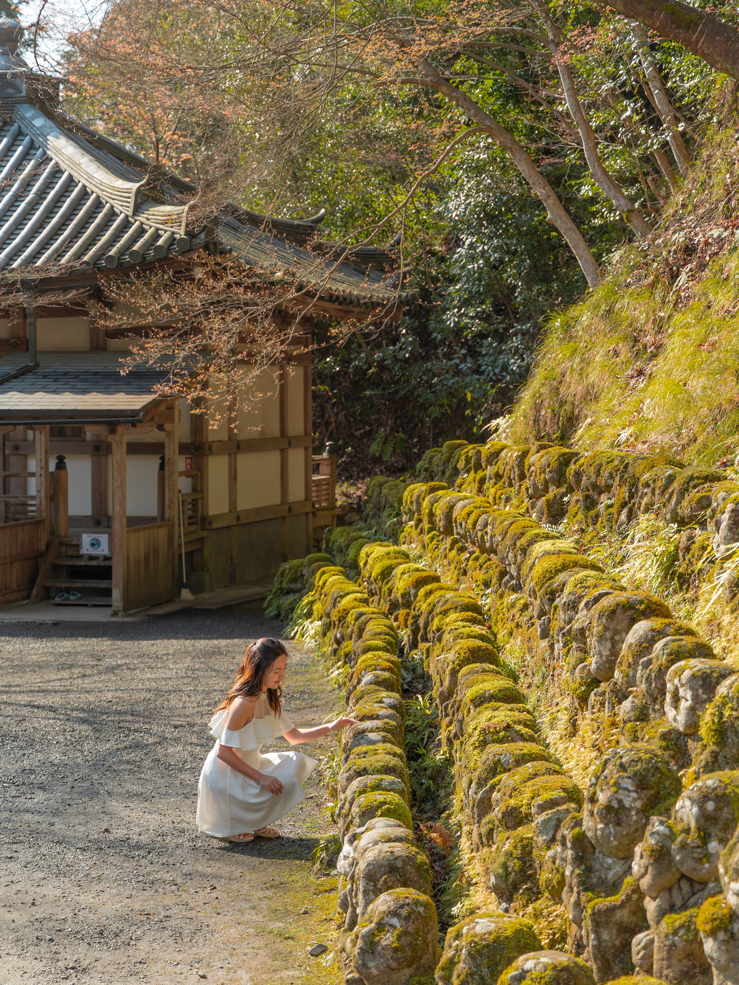 Crouching beside rows of moss-covered rakan statues at Otagi Nenbutsu-ji temple in Arashiyama