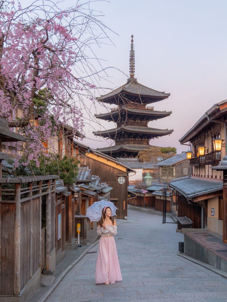 Yasaka Pagoda rising above traditional Kyoto rooftops with weeping cherry blossoms at dusk