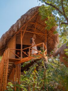 Woman standing on the balcony of a thatched-roof treehouse at Mizata by Antiresort in El Salvador