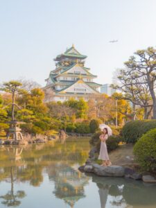 Woman with parasol by the reflecting pond at Osaka Castle garden with the castle in the background