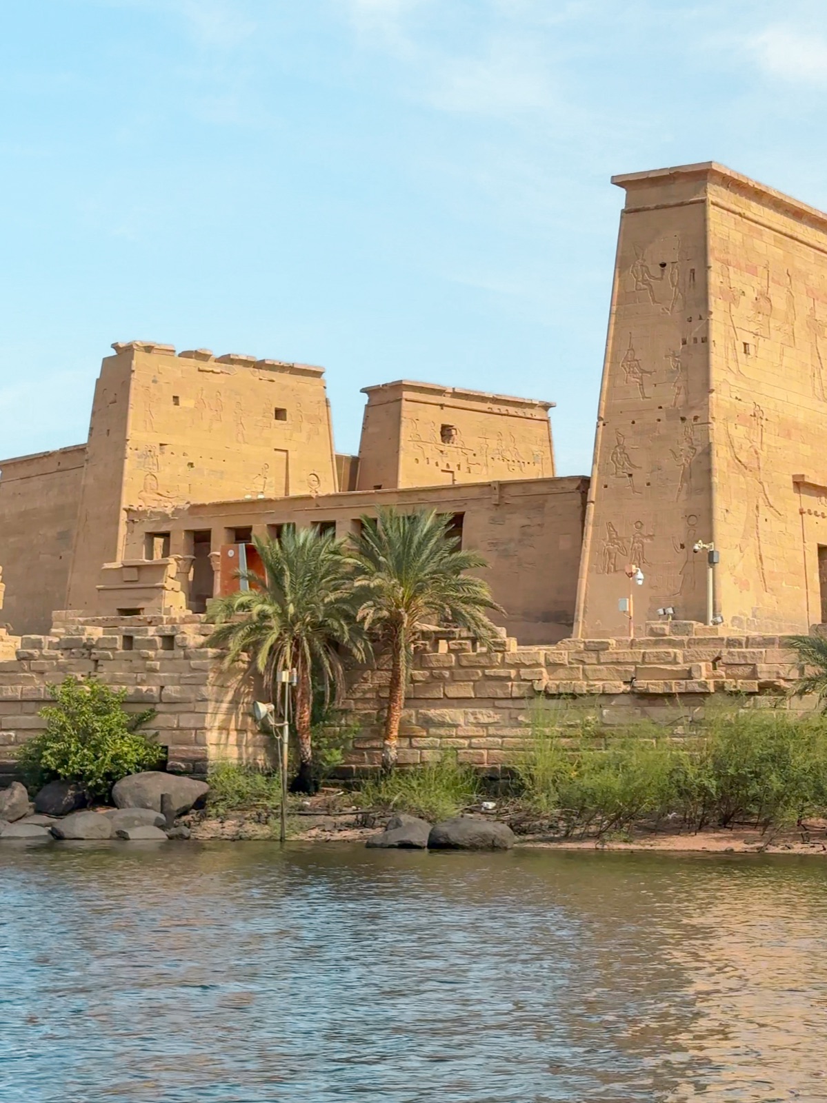 Philae Temple towers and palm trees on the island shore, viewed from the Nile