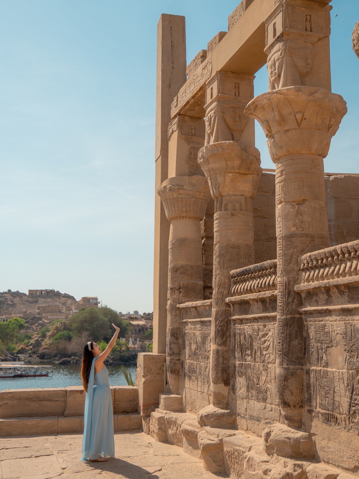 Woman in a blue dress beside columns at Philae Temple with the Nile behind her