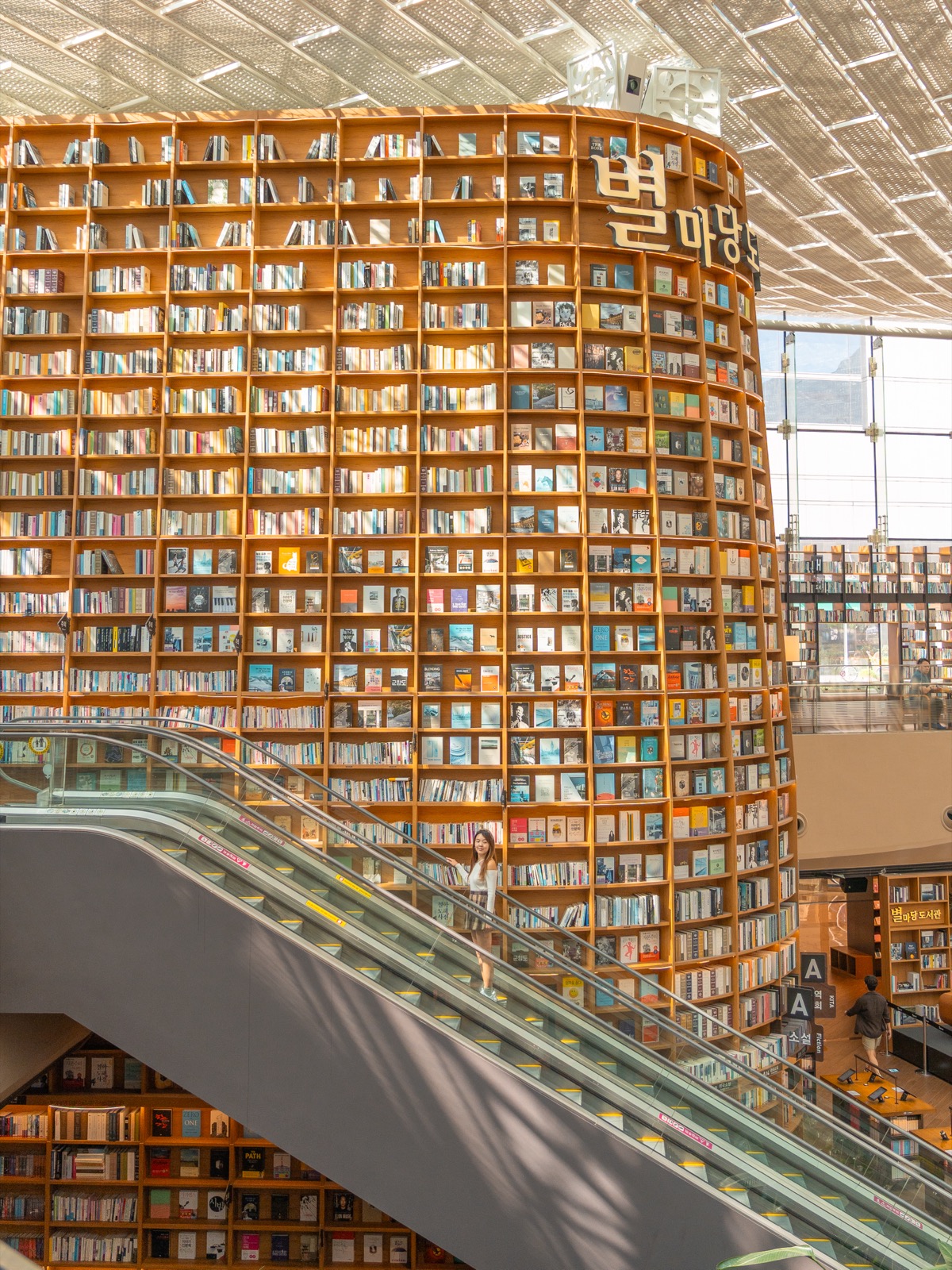 Woman on escalator beside the towering bookshelves of Starfield Library inside COEX Mall in Seoul, South Korea