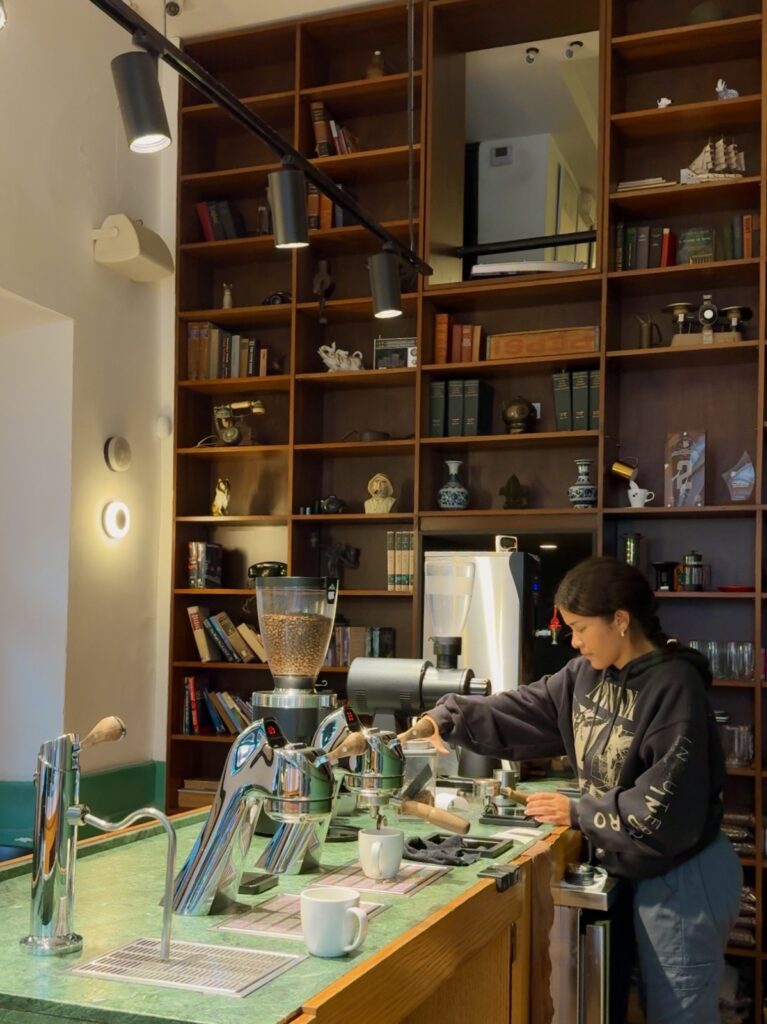 Barista making coffee behind a green marble counter with floor-to-ceiling wooden bookshelves at Unido Coffee in Casco Viejo, Panama